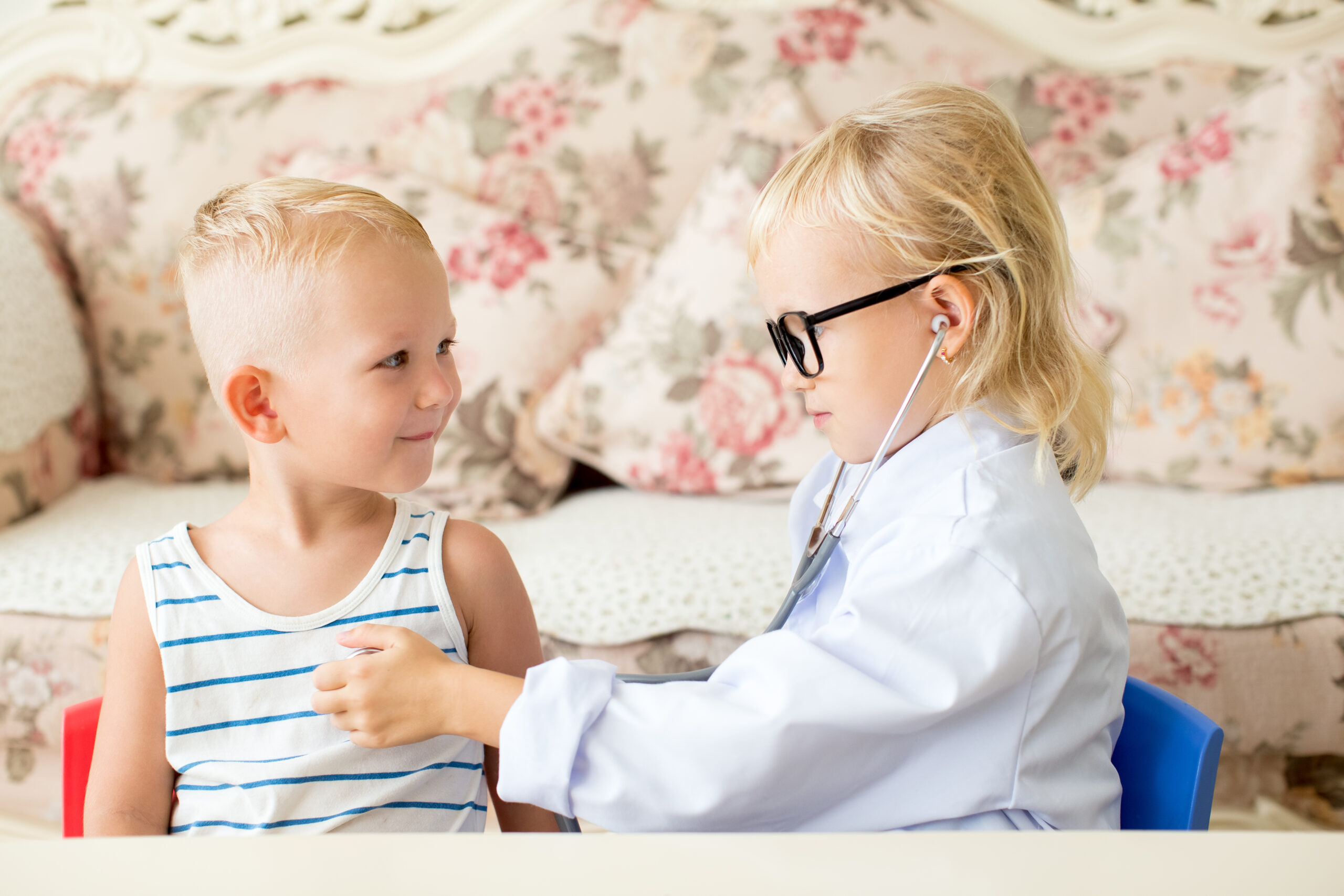 Portrait of serious little girl playing doctor examining boy patient with stethoscope. Occupation, health and childhood concept