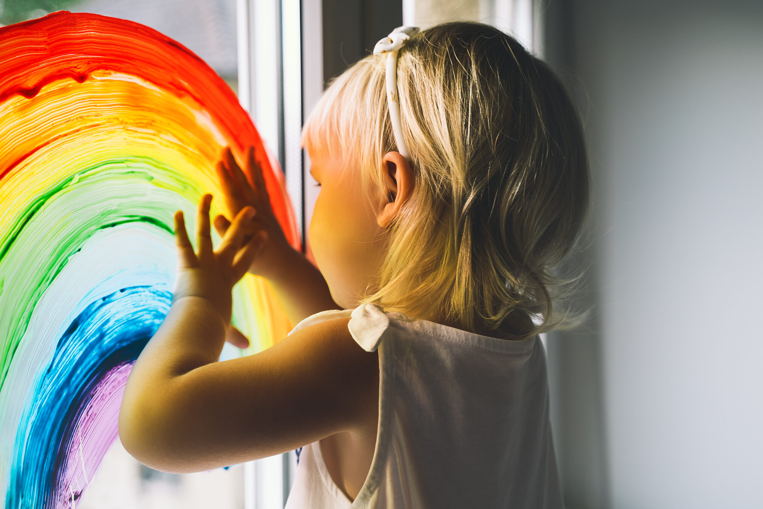 Little girl hands touch painting rainbow on window. Child Art and Creative. Kids leisure at home, childcare, safety joy symbol. Positive visual support during quarantine Coronavirus Covid-19 at home.
