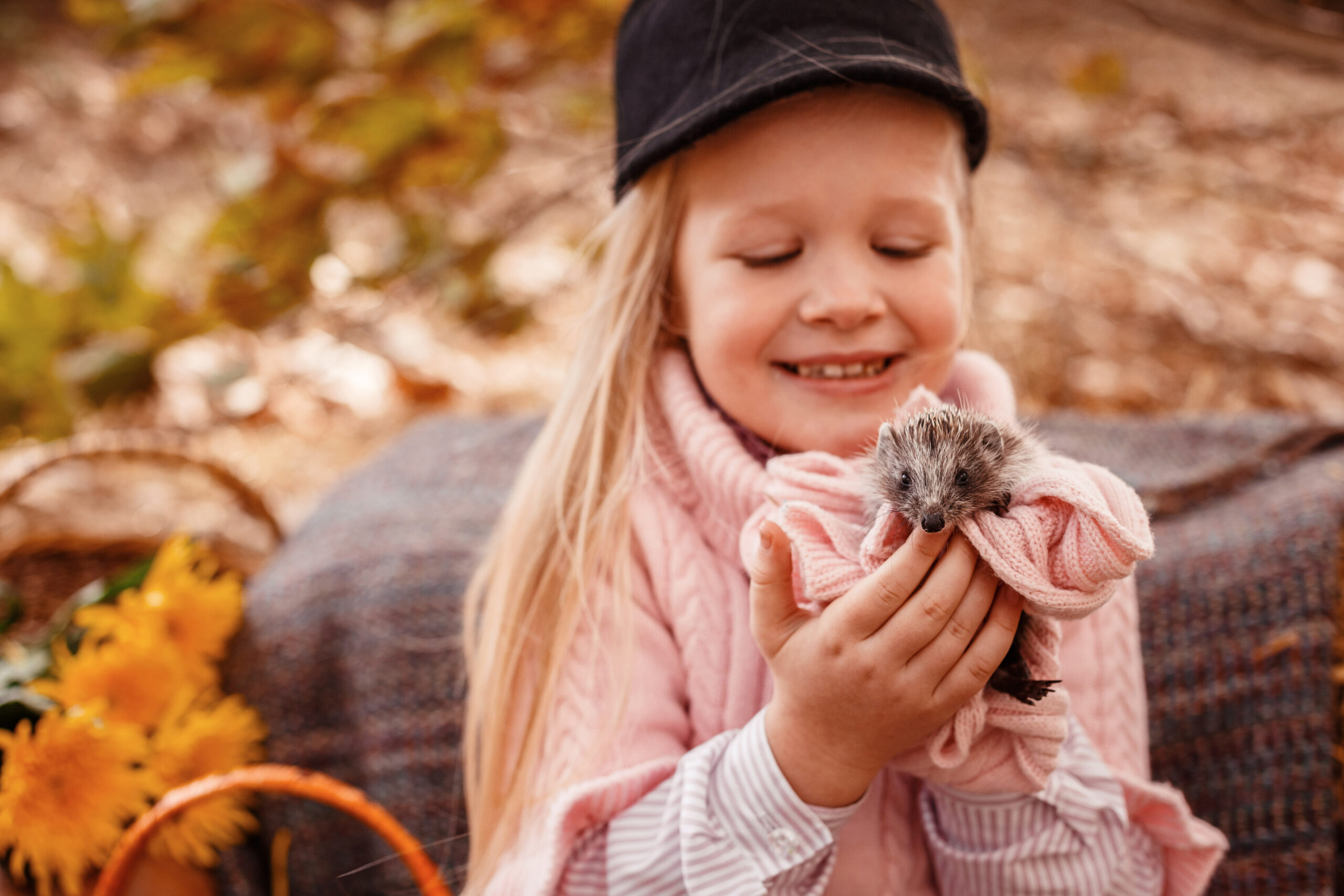 Happy little child girl with cute hedgehog. Portrait of kid with pet in autumn nature, with pumpkins and straw, holding a cup of hot drink